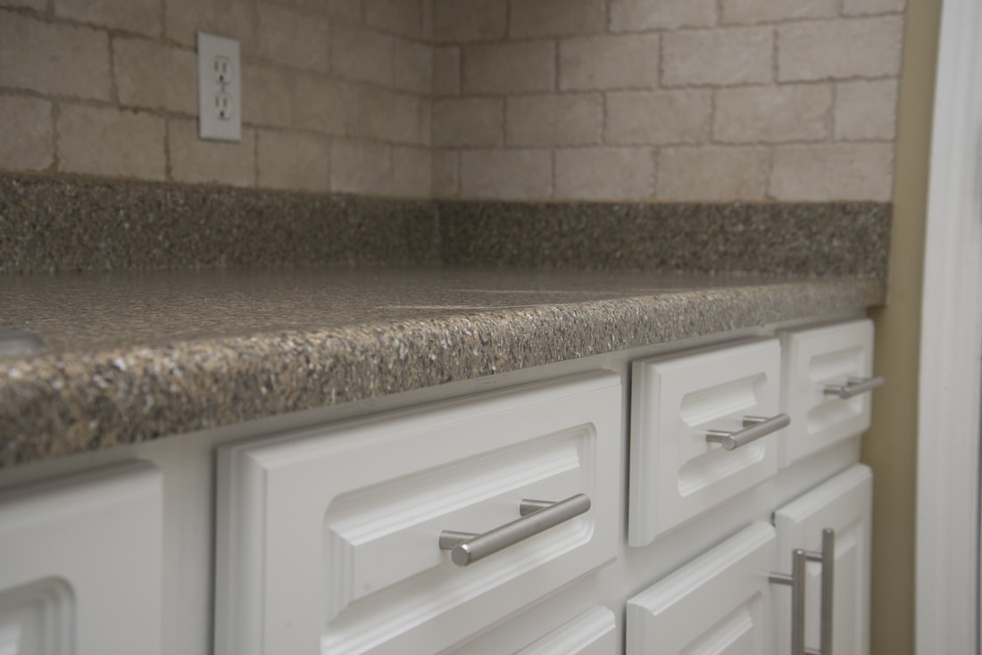 Close-up of a kitchen countertop with textured stone surface and white cabinets with silver handles underneath.