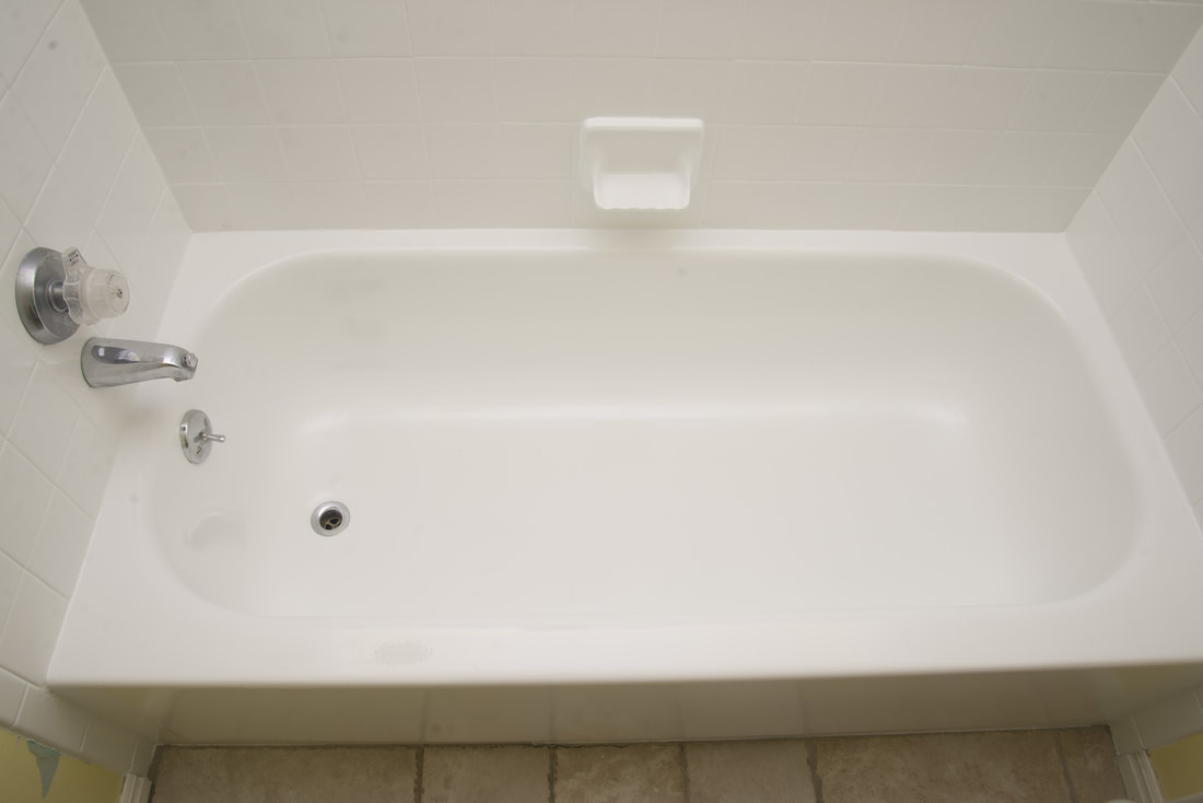 Empty white bathtub with silver faucet and white tiled walls, beige tiled floor.